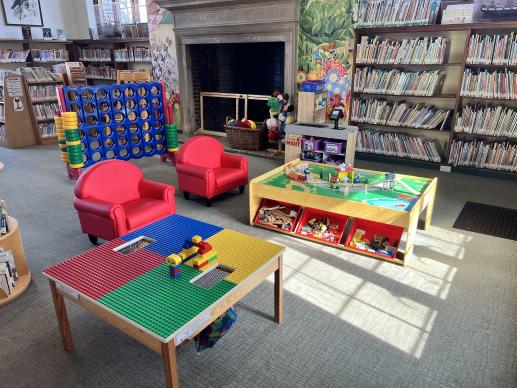 Play area which includes a lego table, train table, and play grocery area. Pictured in the back is a large connect four