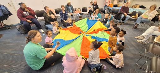 Children sitting on the floor around a parachute.