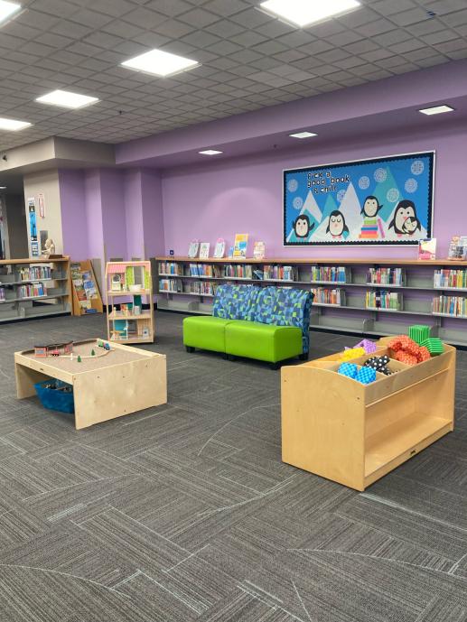 Photo of children's area featuring soft blocks, doll house, train table, reading chairs, and bulletin board